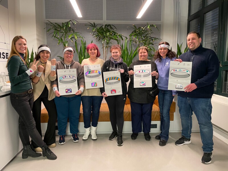 In the photo there are several people showing their results of the inclusive design workshop. They all look joyful.