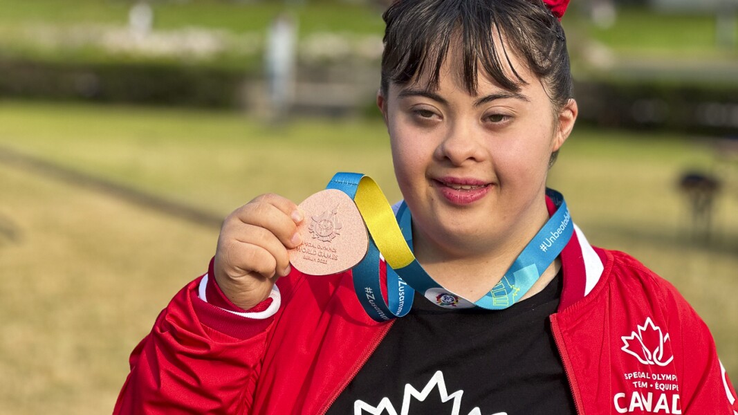 The photo shows a rhythmic gymnastics athlete with her medal in hand. She smiles into the camera.