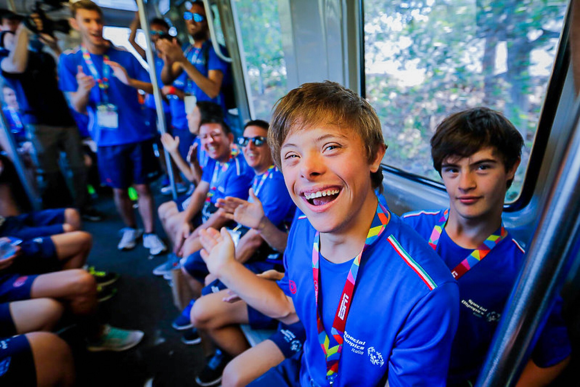 The photo shows athletes of the Italian delegation on a train. They laugh into the camera and are happy.
