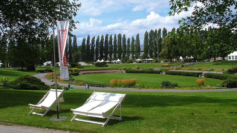 The photo shows the Sommergarten, which is located within the fair grounds of Messe Berlin. In the foreground are deck chairs and in the background stretch wide meadows and paths.