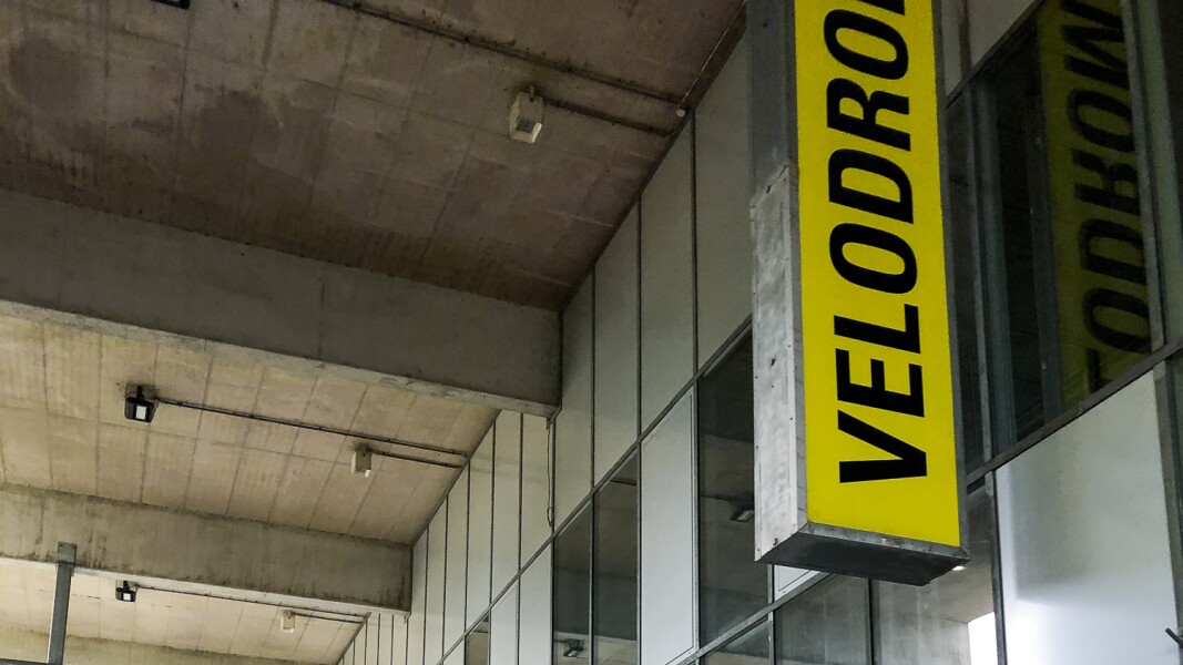 Das Foto zeigt den Eingangsbereich des Velodroms vor dem auf einem großen gelben Banner die Aufschrift "VELODROM" senkrecht von unten nach oben verläuft.